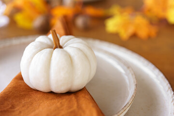 White decorative pumpkin on orange napkin on table autumn setting for fall holidays in warm tones