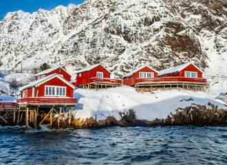 A i Lofoten village with traditional red wooden fishermen cabins on stilts in water, called rorbu, on Lofoten islands in winter. Snowy Scandinavian landscape in northern Norway