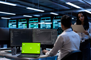 Teamworking technicians in server room using green screen laptop to find network issues affecting supercomputers. IT experts fixing slow data transfer rates in data center with chroma key notebook