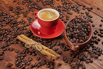 Cup of coffee in the foreground with roasted coffee beans and a cinnamon stick against a background of old wood