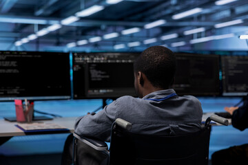 African american person with paraplegia working in inclusive server room workplace, typing on PC....