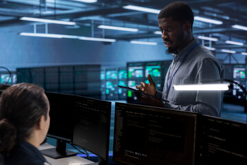 African american man in data center using diagnostic tools and system monitoring software to identify root cause of errors. Supervisor in server room overseeing employee repairing equipment