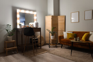 Interior of makeup room with glowing mirror, table and sofa