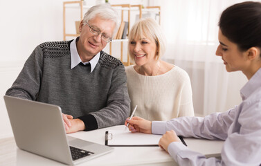 Older couple considering new home purchase talking with real estate agent and looking at laptop