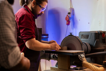 Carpenter in woodworking shop wearing protection glasses while shaping wooden object on disc...