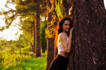 Beautiful happy slim healthy sport body woman posing in fashion clothing hugging huge tree on...