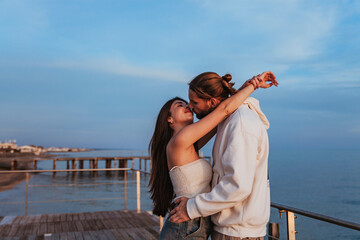 young engaged couple kissing passionately. They are both dressed in white and are on the shore of a beach at sunset	