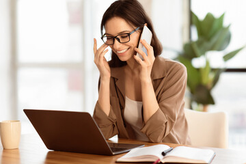 Informal Call. Excited european secretary in glasses talking on mobile phone at coffee break sitting at office, copyspace