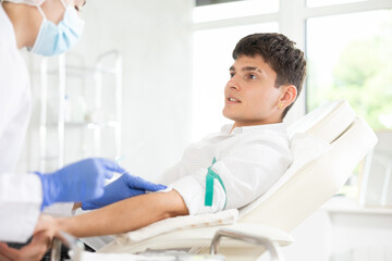 Fototapeta premium Nurse giving intravenously injection to young brown-haired boy lying at exam room of clinic