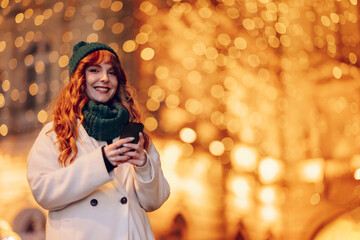 A happy woman is using cellphone on street on christmas eve.