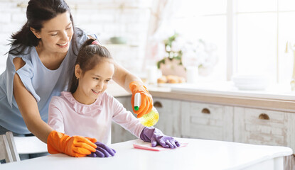 Caring mom in rubber gloves teaching daughter how to clean table with detergent, panorama with copy space
