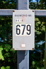 Schild mit einer Bauwerksnummer an einem Geländer. Bauwerksnummern dienen in Deutschland zur...