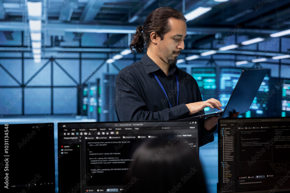 Poster engineer standing in data center, typing on laptop, doing yearly checkup to avoid equipment downtime