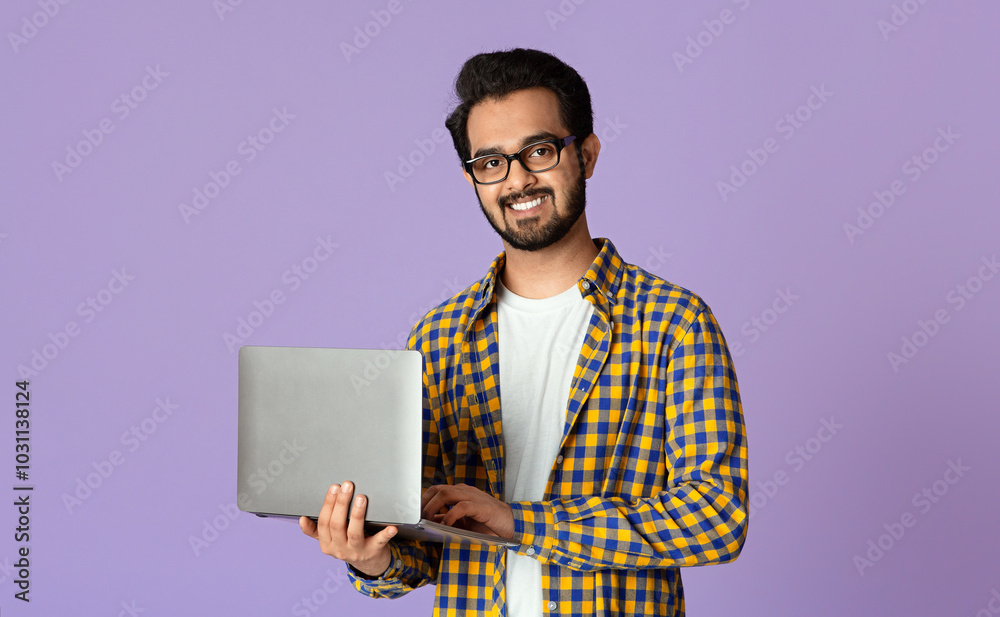 Poster happy indian guy with laptop computer working or studying online on lilac background