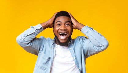 Wow. Excited african american guy holding hands on head, looking at camera with amazement, yellow...