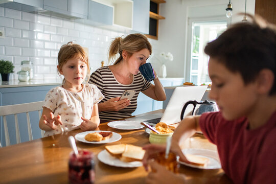 Mother working on laptop while family has breakfast in kitchen