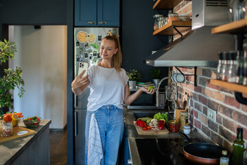 Smiling young woman using smartphone in modern kitchen