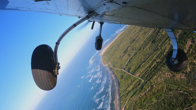 Light three wheels training airplane doing exercises in the air. Performance steep turns to left and right. Fly overhead green field following coastline to the ocean. View from bottom of aircraft.