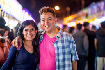 Close-up of a beautiful Latin couple taking a photo in the middle of the street at night. They have visited the fair in their city.