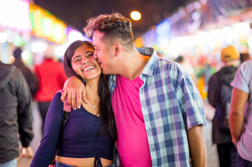 The loving boyfriend kisses his girlfriend during the walk they take at night, both enjoying the attractions of the night ride.