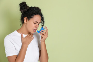 Young woman using asthma inhaler on light green background. Space for text