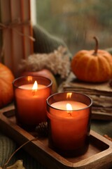 Burning candles, books and autumn decor on sweater near window, closeup