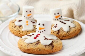 Delicious cookies with snowmen made of marshmallows on white table, closeup