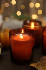 Burning candle and autumn decor on wooden table, closeup
