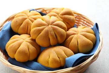 Wicker basket with tasty pumpkin shaped buns on light table, closeup
