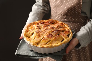 Woman holding tasty homemade apple pie on black background, closeup