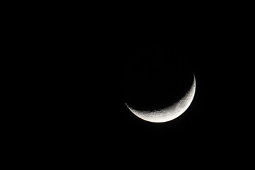 Waning crescent moon against black starless and cloudless sky.