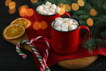 Tasty hot cocoa drinks with marshmallows in mugs and Christmas decor on black wooden table, closeup