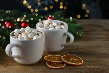 Tasty hot cocoa drinks with marshmallows in cups and dry orange slices on wooden table, closeup