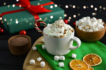 Tasty hot cocoa drink with whipped cream in cup and marshmallows on black wooden table, closeup