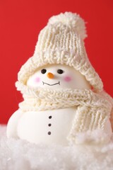 Cute decorative snowman on artificial snow against red background, closeup