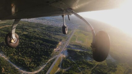 Light three wheels training airplane doing ledt turn from base for the final approach ti airport. Fly overhead greenery. View from the bottom of aircraft.