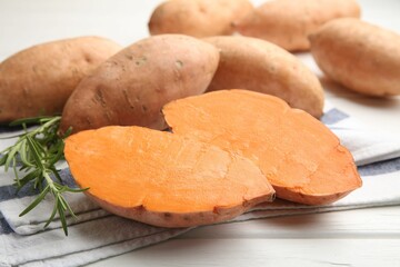 Fresh raw sweet potatoes and rosemary on white wooden table, closeup