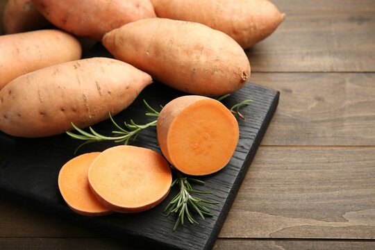 Fresh raw sweet potatoes and rosemary on wooden table, closeup