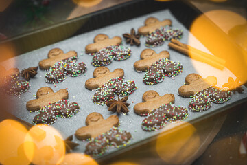 Three rows of gingerbread men with chocolate and sprinkles on white baking paper in a baking dish with cinnamon.