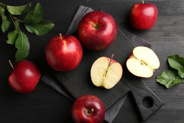 Fresh ripe red apples and green leaves on black wooden table, flat lay