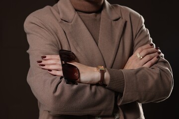 Woman with sunglasses in stylish coat on brown background, closeup