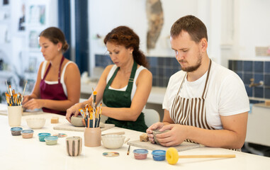 Three pottery workers mold clay into homemade plates and other utensils.