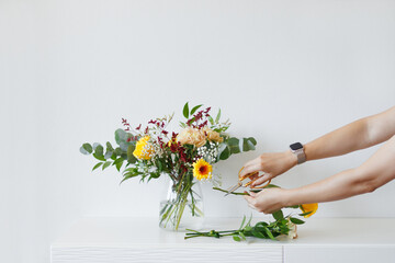 Florist Cutting Flower Stems While Preparing A Floral Arrangement  For Bouquet Design In A Vase On A White Table