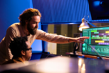 Sound engineer collaborating with singer to edit sounds and compose songs in control room at...
