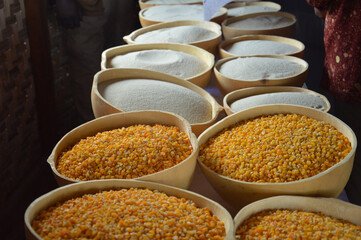Baskets filled with vibrant yellow corn kernels and finely milled white flour are displayed on a market stall,