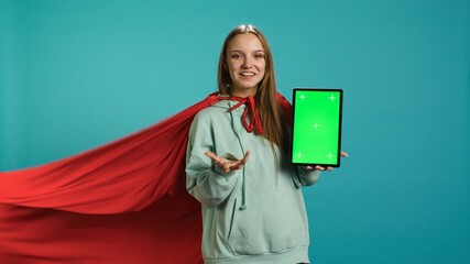 Woman wearing superhero costume presenting and talking about isolated screen tablet, studio...
