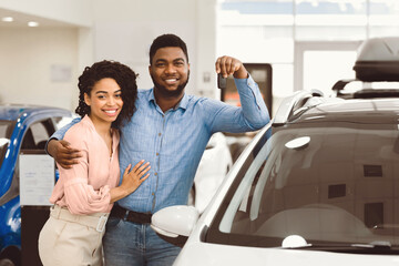 Cheerful African Spouses Holding Car Key Standing Near New Family Automobile In Dealership Center. Copy Space