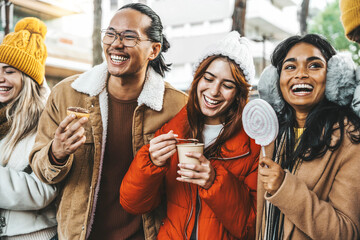 Happy friends having fun drinking mulled wine and hot chocolate at Christmas Market - Young people wearing winter clothes walking in city street
