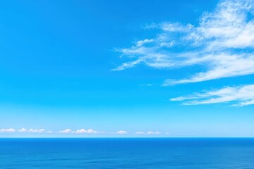 Obraz premium A serene view of the endless ocean under a bright blue sky with wispy clouds, evoking tranquility and peace.