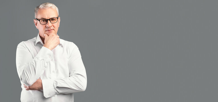 Making Decision. Portrait of pensive mature man in glasses looking at camera isolated over gray studio wall